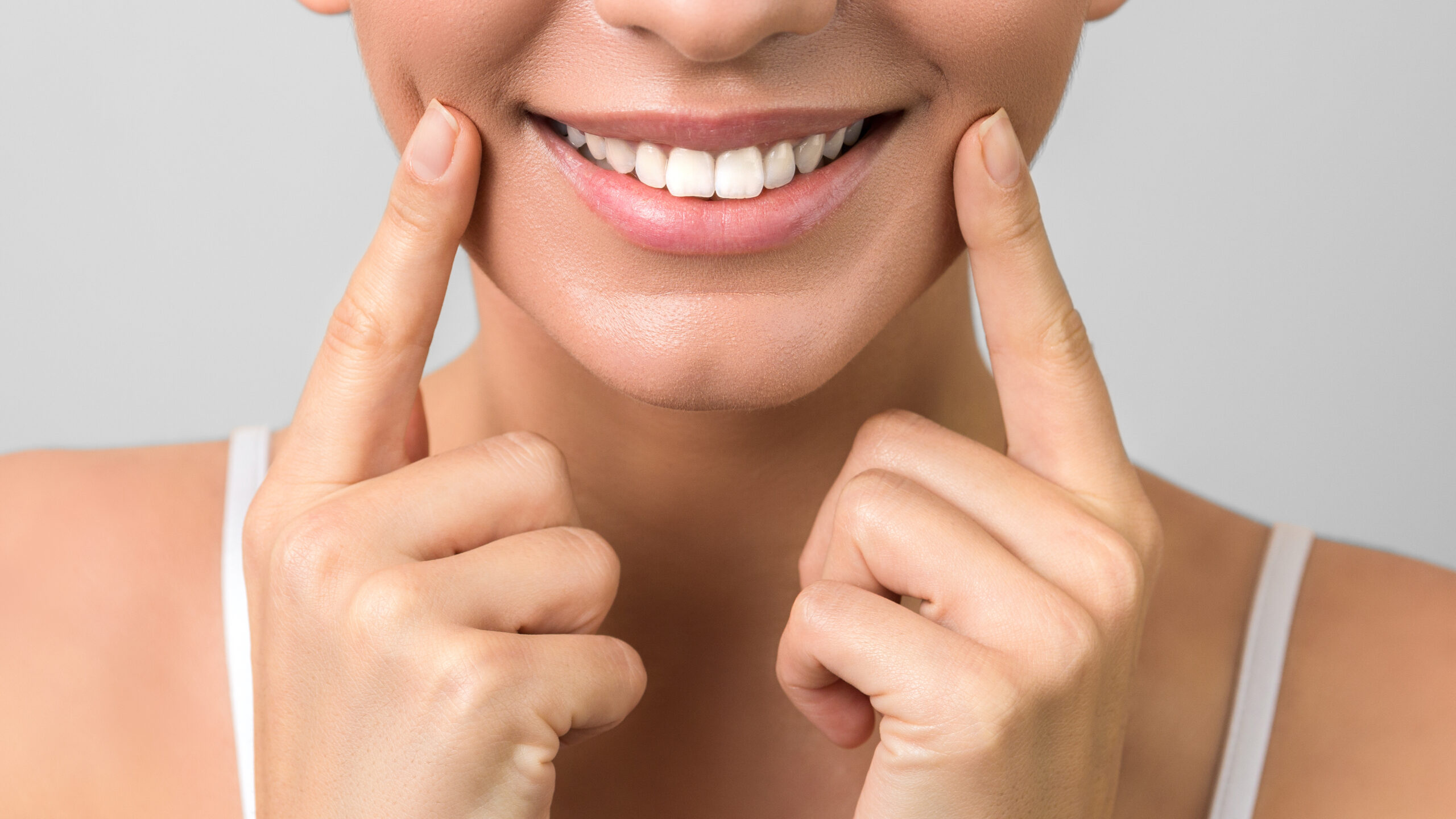 closeup beautiful healthy smile and white teeth of a young attractive woman on grey background